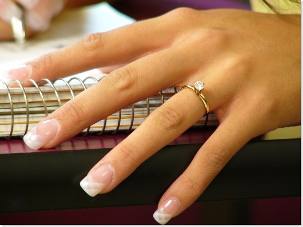 Woman's hand wearing an enagement ring resting on a desk