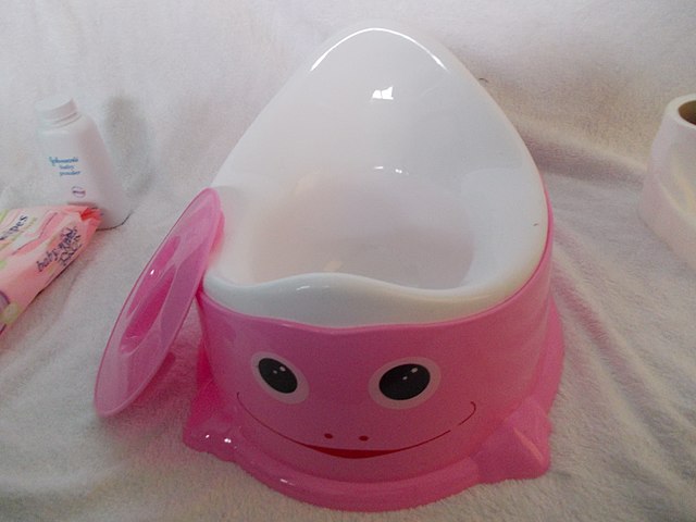 Pink frog-design potty with baby wipes and baby powder in the background.