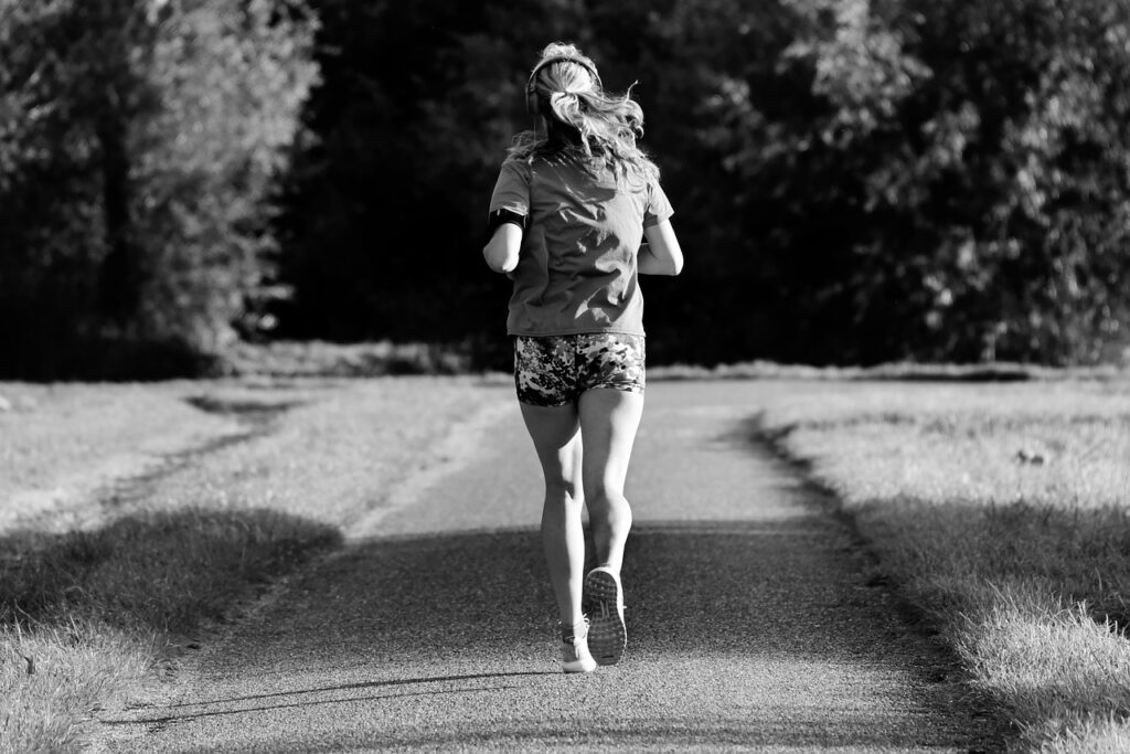 Black and white photo of a woman running through a park wearing shorts and a t-shirt.