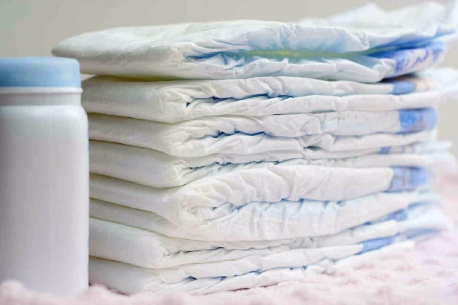 A stack of white diapers or nappies, with a bottle of baby powder.