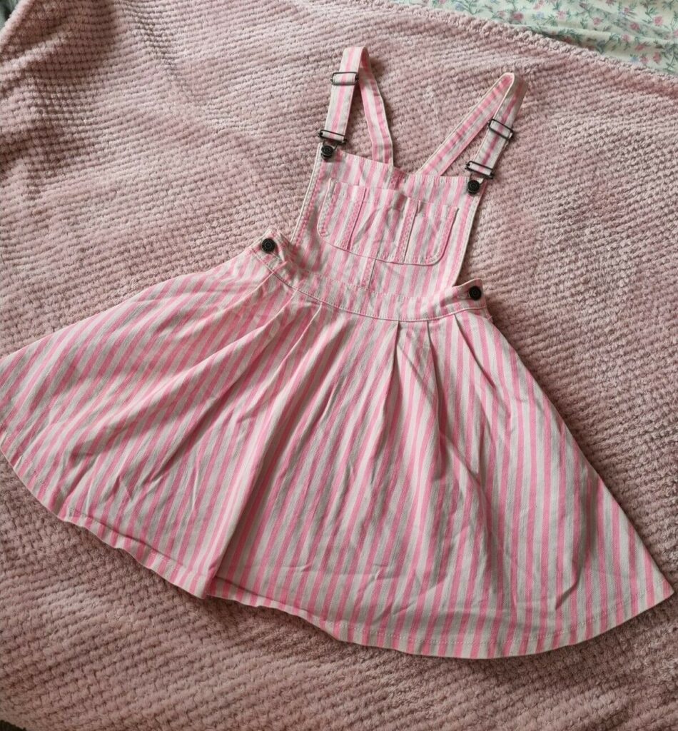 A pink dungaree dress with white stripes.