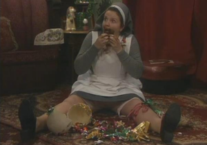A nun sits in the middle of a pile of empty Easter egg boxes. She looks guilty. There is chocolate around her mouth.