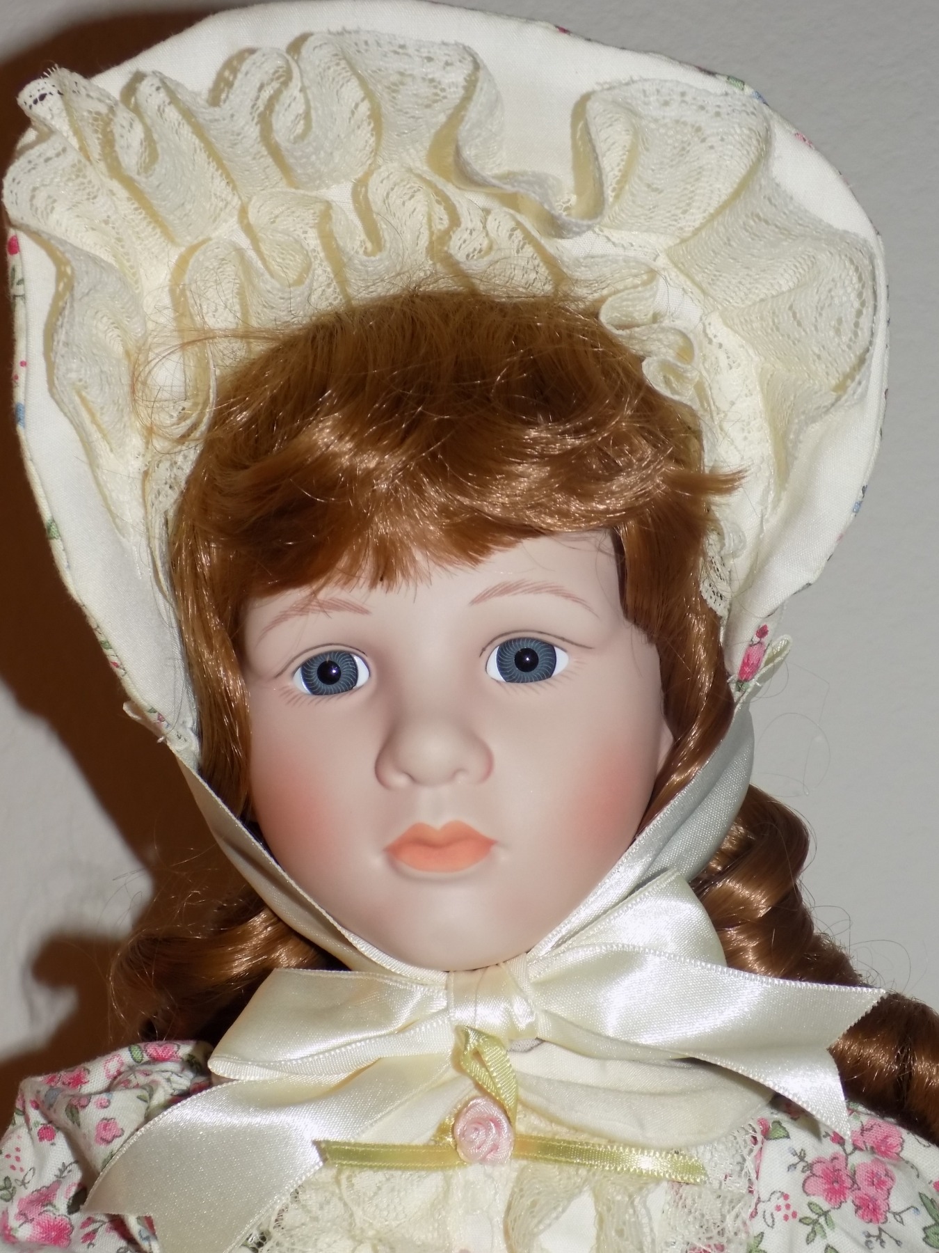 A sad Victorian doll with a frilly bonnet and curly hair.